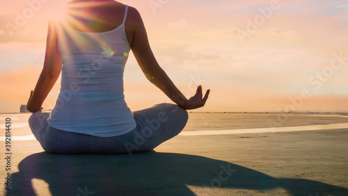 Back view young woman hand meditation lotus pose in sunlight mood on the rooftop building and evening sky scene with city background