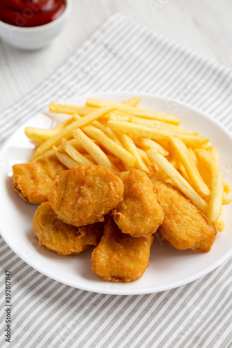 Tasty Fastfood: Chicken Nuggets and French Fries on a plate on a white wooden surface, side view. Close-up.