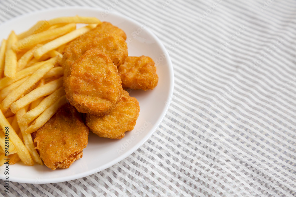 Tasty Fastfood: Chicken Nuggets and French Fries on a plate on cloth, low angle view. Space for text. Tasty Fastfood: Chicken Nuggets and French Fries on a plate on cloth, low angle view. Space for text.