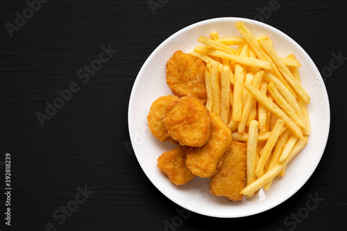 Tasty Fastfood: Chicken Nuggets and French Fries on a plate on a black surface, top view. Flat lay, overhead, from above. Copy space.
