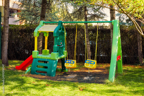 Children playground with plastic swings and slide on the grass of a garden