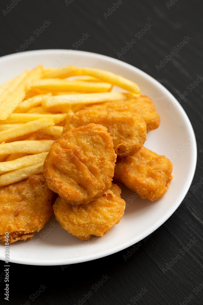 Tasty Fastfood: Chicken Nuggets and French Fries on a plate on a black background, side view. Close-up. Tasty Fastfood: Chicken Nuggets and French Fries on a plate on a black background, side view. Close-up.