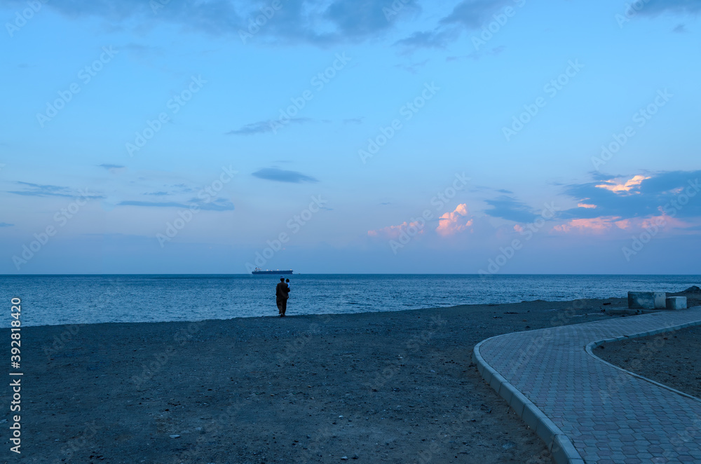 An Omani Man & child looking at a ship in the distance in the evening at Darsait beach, Muscat, Oman. An Omani Man & child looking at a ship in the distance in the evening at Darsait beach, Muscat, Oman.