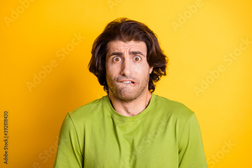 Photo of afraid young man bite lip anxious look camera wear green t-shirt isolated yellow color background