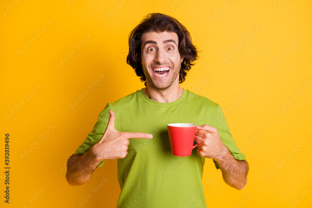 Portrait photo of man pointing with finger at red cup of tea smiling cheerfully isolated on bright yellow color background