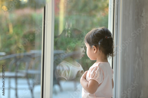 Sad asian little girl looking outside through the window
