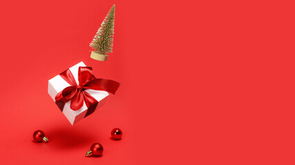 Holiday Christmas background. Golden winter tree, white gift box with red ribbon falling with balls and sparkling lights on reddish background for greeting card. Christmas, winter, new year concept.