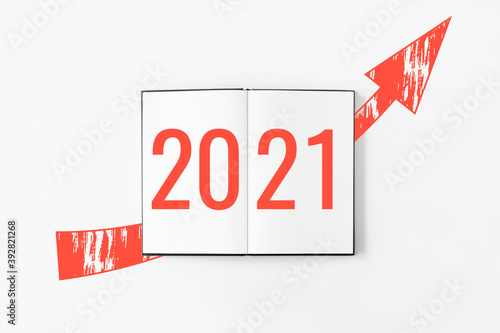 2021 on notebook with red arrow rising up flat lay on white background. New year resolutions. Money, business success. Financial progress. Purpose for 2021. Goals, plans, projects, ideas.