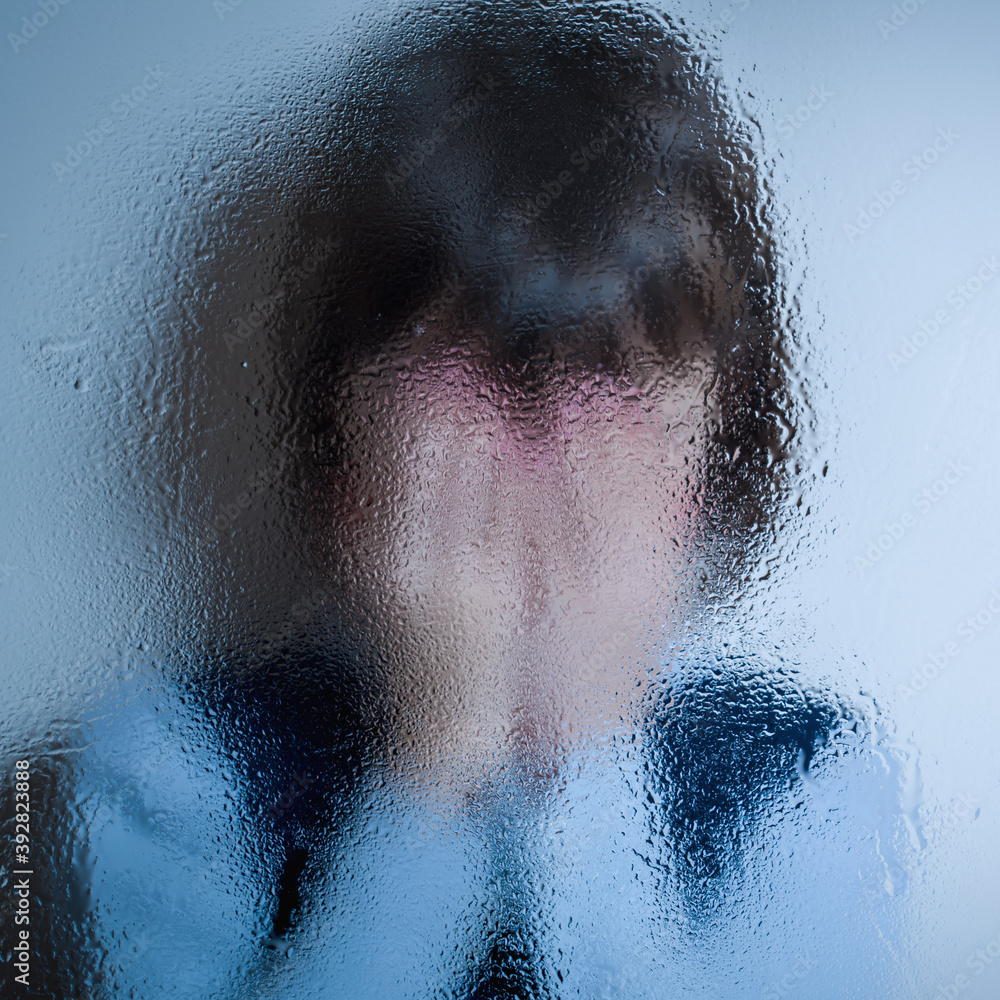 Children's fear and anxiety, psychological violence and pain. Little chidn girl covered her face with palms and cries behind wet glass. Selective focus.