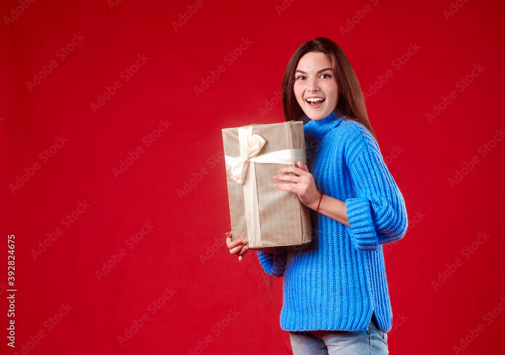 girl in a blue sweater holding a gift in her hands on a red background. girl in a blue sweater holding a gift in her hands on a red background.