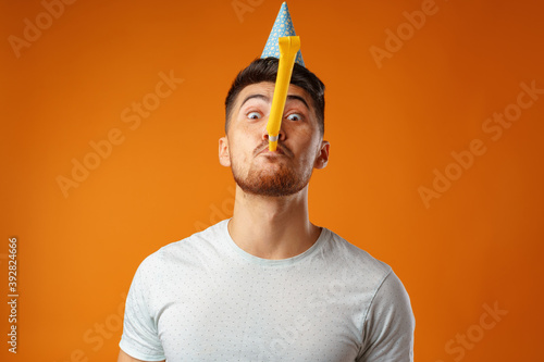 Happy man with party cone blowing into party horn