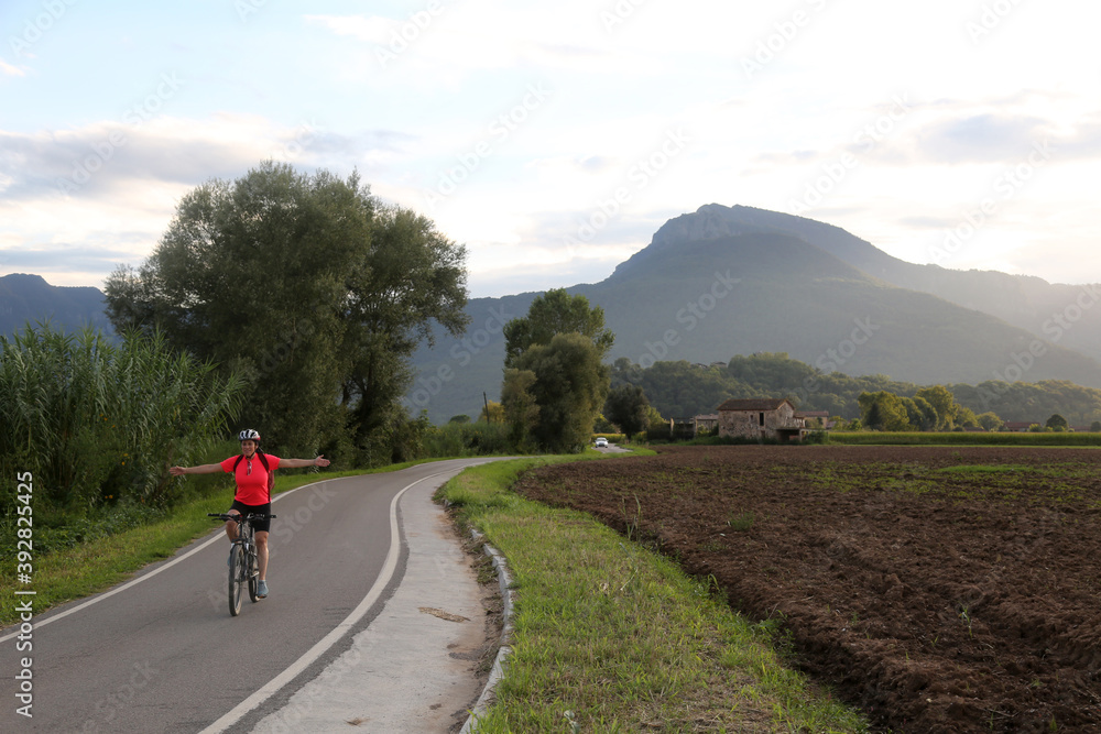 Woman biking in countryside in a narrow road with mountain background