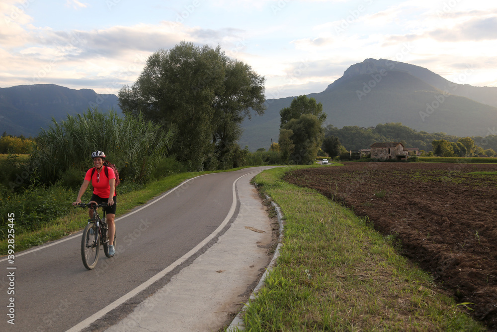 Woman biking in countryside in a narrow road with mountain background Woman biking in countryside in a narrow road with mountain background