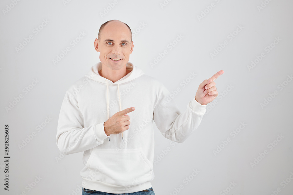 Studio portrait of smiling mature man in white hoodie pointing away Studio portrait of smiling mature man in white hoodie pointing away