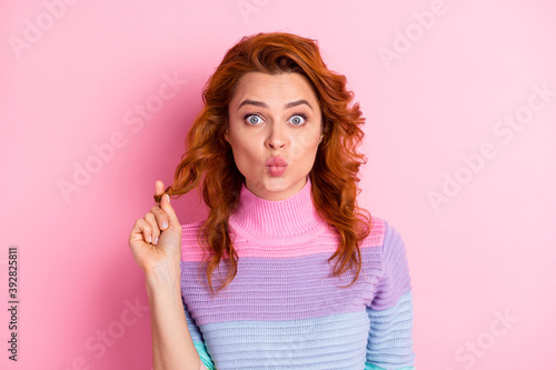 Photo portrait of pouting woman playing with hair isolated on pastel pink colored background