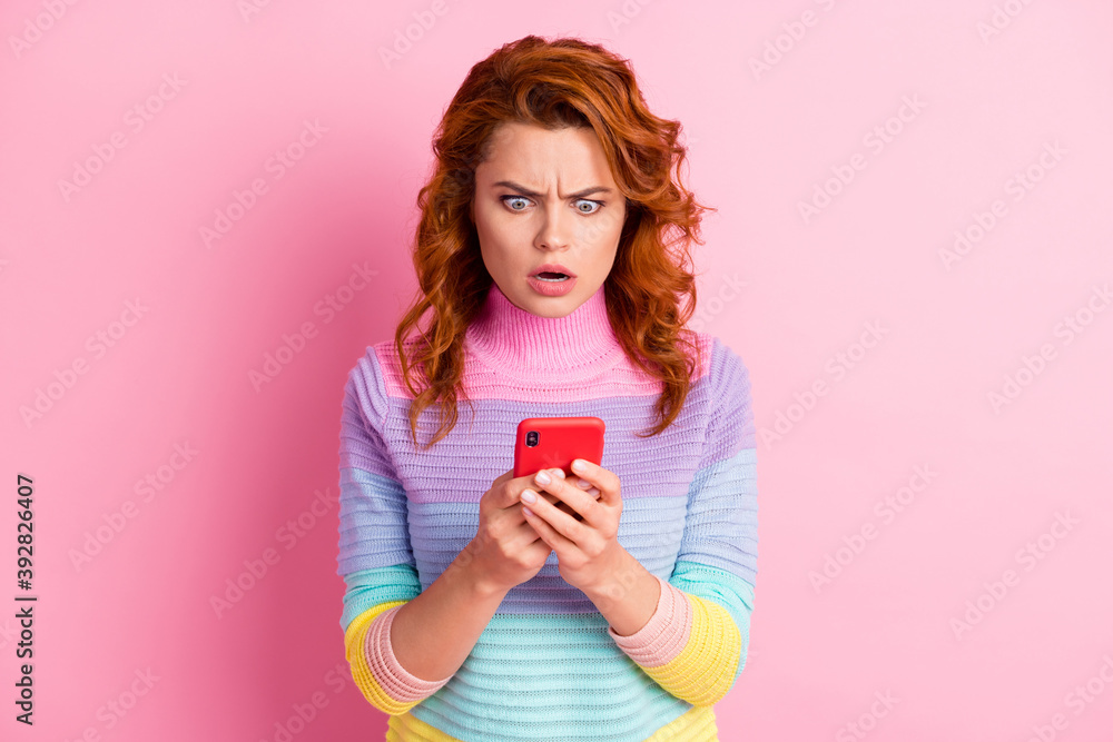 Photo portrait of shocked angry woman holding phone in two hands isolated on pastel pink colored background Photo portrait of shocked angry woman holding phone in two hands isolated on pastel pink colored background