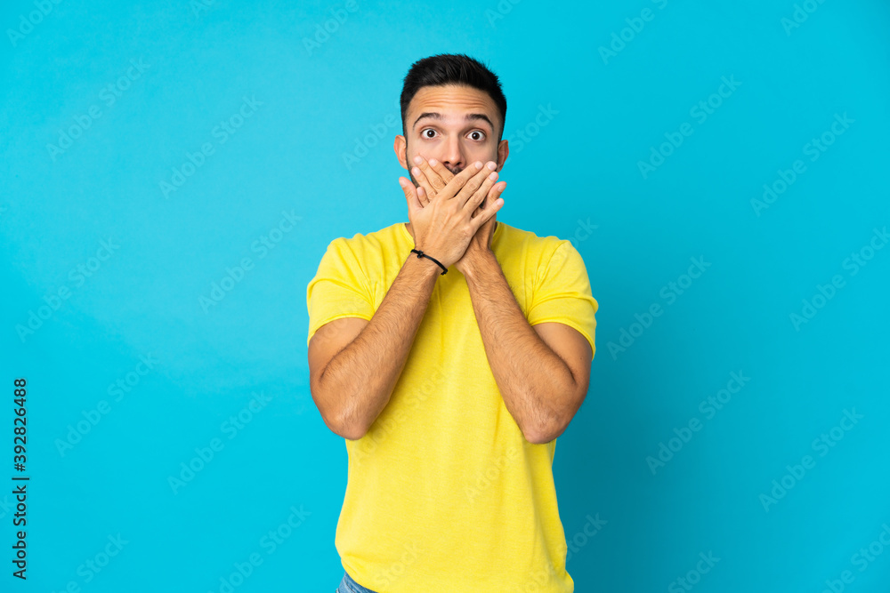 Young caucasian man isolated on blue background covering mouth with hands Young caucasian man isolated on blue background covering mouth with hands