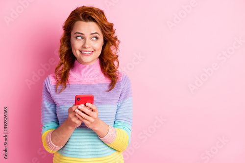 Photo portrait of woman holding phone in two hands looking at blank space isolated on pastel pink colored background