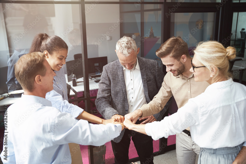 Obraz premium Celebrating success. Group of happy multiracial business people doing fists bump while standing in the office