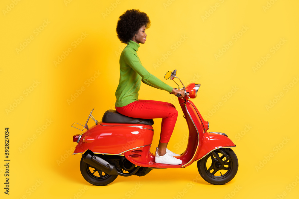 Photo portrait of brunette african american woman riding red motorbike isolated on vivid yellow colored background Photo portrait of brunette african american woman riding red motorbike isolated on vivid yellow colored background