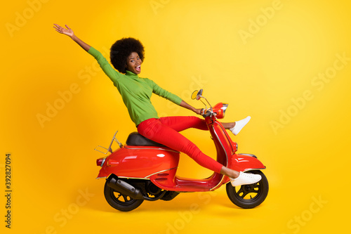 Photo portrait of african american woman riding bike waving hand with spread legs open mouth isolated on vivid yellow colored background