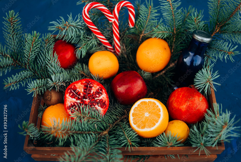 Christmas composition in a wooden basket with fruits, lollipops and a Christmas tree on a blue background Christmas composition in a wooden basket with fruits, lollipops and a Christmas tree on a blue background