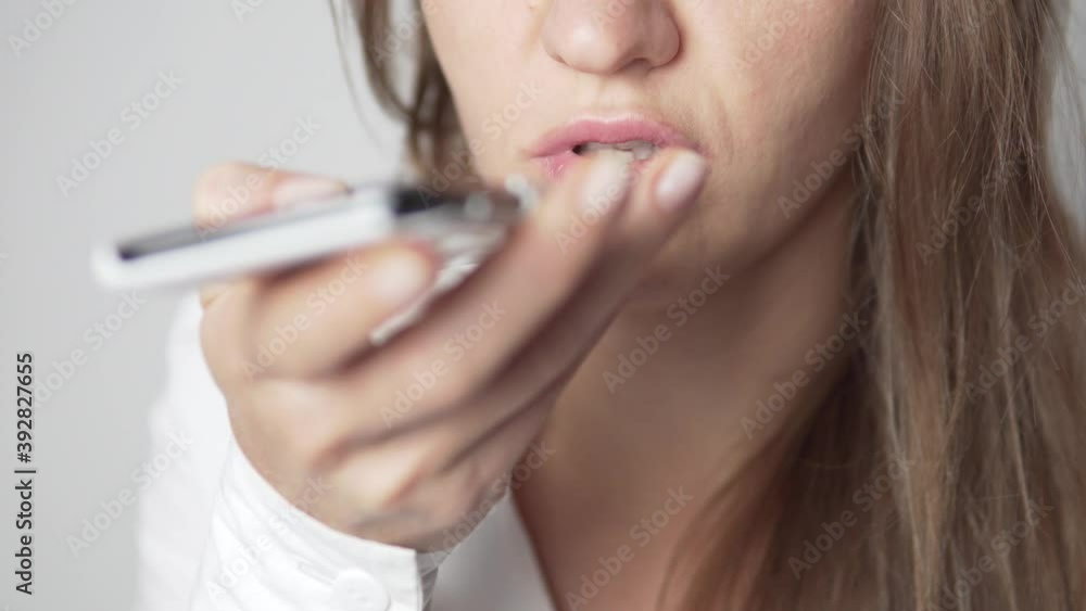 A businesswoman in a white shirt records an audio message on a mobile phone. Focus on a woman's face, the phone is blurred. A businesswoman in a white shirt records an audio message on a mobile phone. Focus on a woman's face, the phone is blurred.