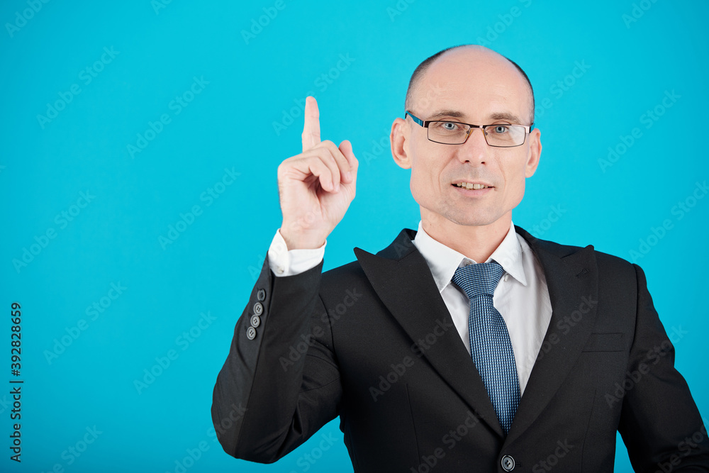 Portrait of confident businessman in glasses smiling at camera, raising index finger and looking at camera Portrait of confident businessman in glasses smiling at camera, raising index finger and looking at camera