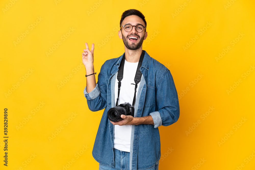 Young photographer girl isolated on yellow background smiling and showing victory sign Young photographer girl isolated on yellow background smiling and showing victory sign