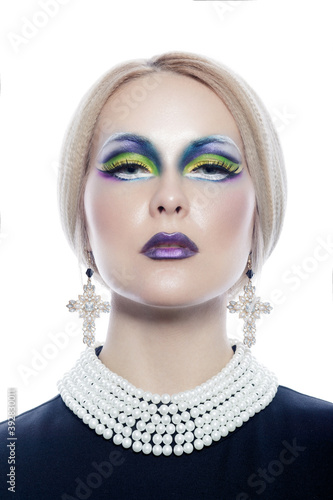 Studio portrait of a beautiful girl with blonde hair and a fashion make-up and pearl necklace and cross earrings.