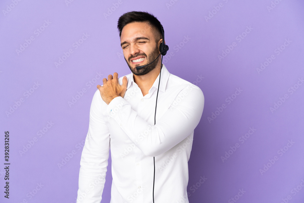 Telemarketer man working with a headset isolated on purple background suffering from pain in shoulder for having made an effort Telemarketer man working with a headset isolated on purple background suffering from pain in shoulder for having made an effort