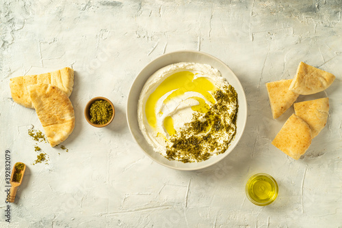 Popular middle eastern appetizer labneh or labaneh, soft white goat milk cheese with olive oil, hyssop or zaatar, olives pita bread , on grey table, top view ,flat lay. Close up image.