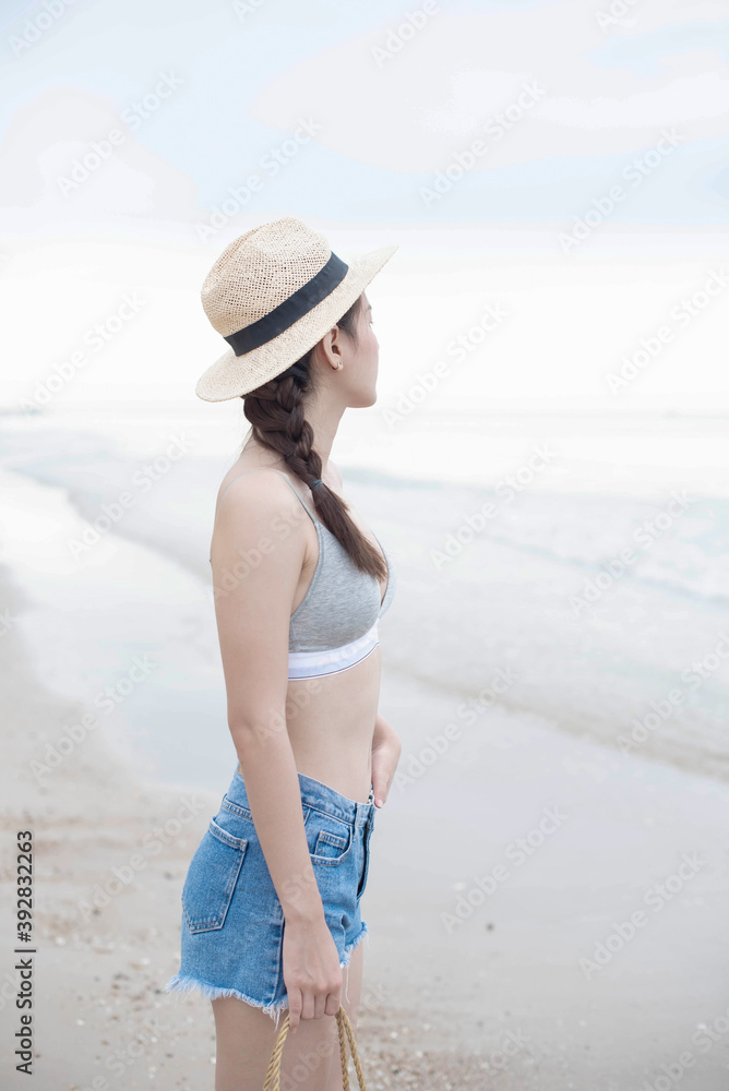 Beach summer holidays woman in happy freedom concept and straw hat. Hot beautiful woman in sunhat and bikini standing with her arms raised to her head enjoying looking view of beach ocean..