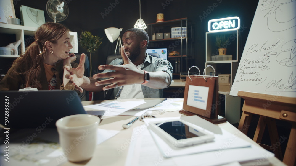 Smiling african american man telling story to businesswoman near laptop indoors.