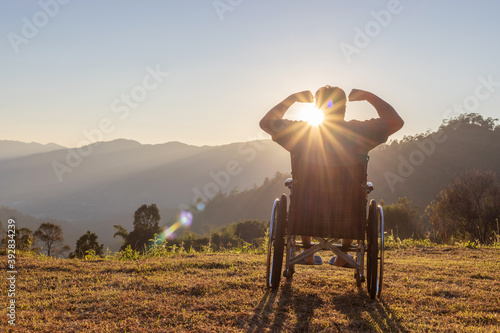 Silhouette of happy disabled man in a wheelchair and stretching hands at sunset. back view,
