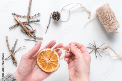 Hands making a homemade Christmas tree toy  from natural eco-friendly materials of dried orange. Top view, flat lay, selective focus.