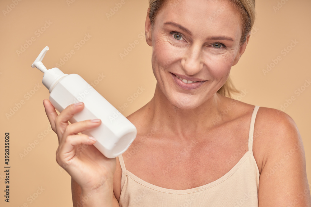 Happy beautiful adult lady showing moisturizing lotion Happy beautiful adult lady showing moisturizing lotion