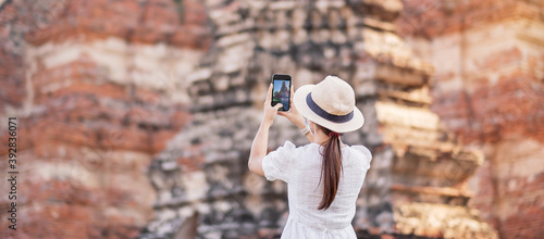 Canvas Print Happy tourist woman wearing surgical face mask and taking Photo by mobile smartphone, protection COVID-19 pandemic during visiting in Ayutthaya temple
