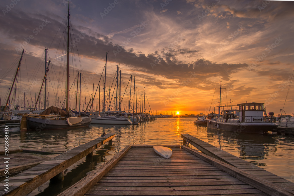 Pier with surfboard at dutch harbour with sailing boats at sunset