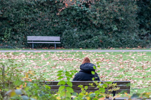 Lonely woman sitting on a park bench isolated with social distancing in corona crisis thoughtful to flatten the curve in the epidemic and pandemic prevention and infection control in fall with leaves photo