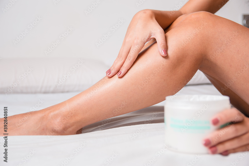 woman sitting on bed putting moisturizer on her legs in her grooming routine woman sitting on bed putting moisturizer on her legs in her grooming routine