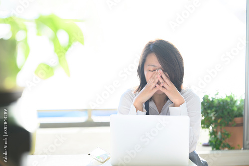 明るい部屋のパソコンの前でカフェの経営に悩んで頭を抱えている30代～40代の日本人女性(主婦)の横向きのコピースペースあり4 photo