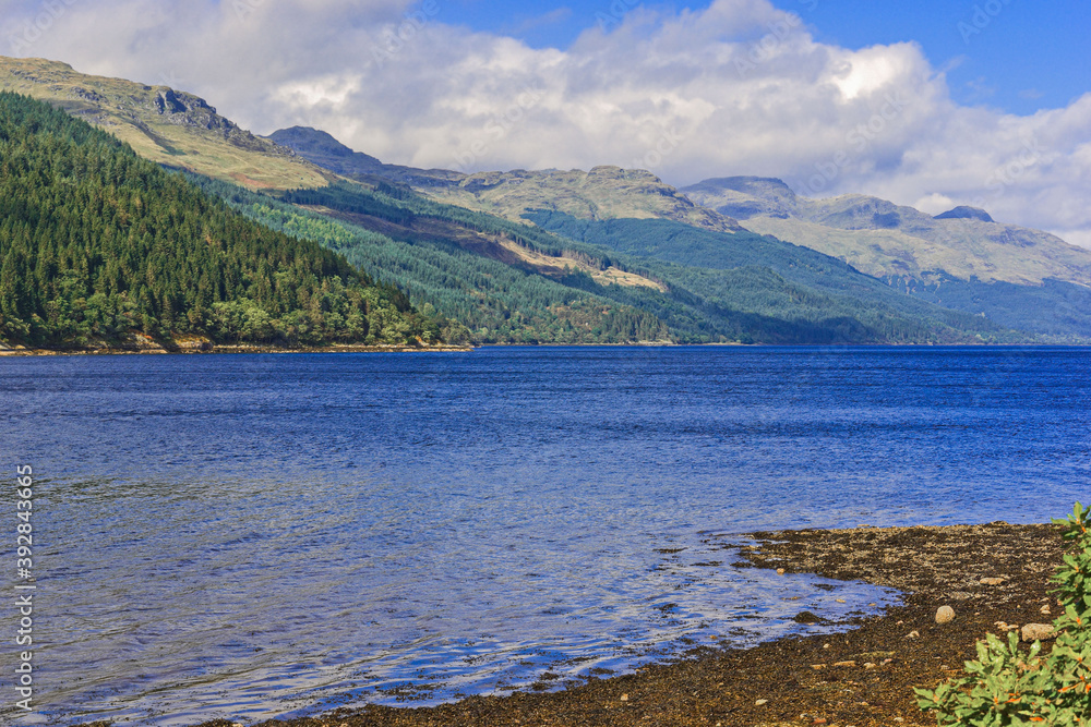 Loch Long, Argyllshire, Scotland. Beautiful Scottish scenery where fluffy white clouds cast shadows over the mountains sweeping down to the sunlit blue waters of the loch.