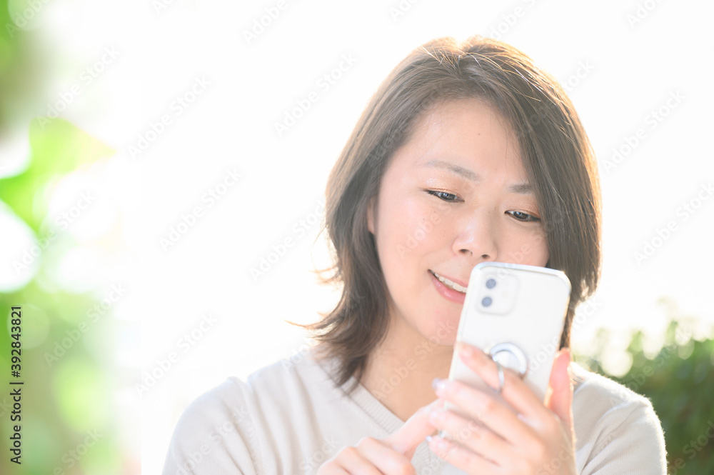 明るい部屋でスマホを見ながらSNSをする30代~40代の日本人の主婦(女性)コピースペースあり 明るい部屋でスマホを見ながらSNSをする30代~40代の日本人の主婦(女性)コピースペースあり