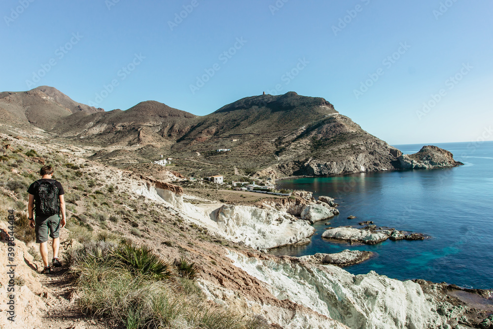 Solo man backpacker hiking along the coast in Andalusia,Spain.Active healthy lifestyle.Majestic view of wild beach,cliffs and seashore.Beautiful mountain summer landscape.Wanderlust travel background.