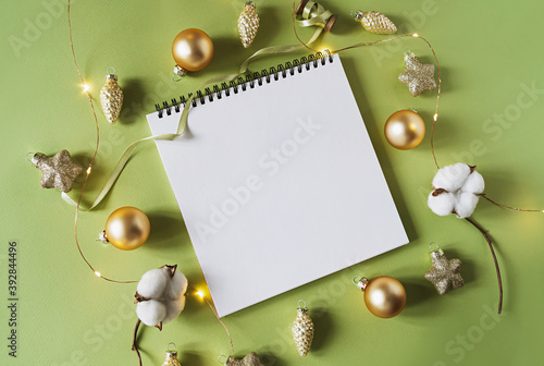 .Christmas festive decorations and notebook. With wish list and 2021 goals concept. Notebook mock up, gift, and coton branch with shiny golden balls.New year flat lay, top view, copy space.. photo