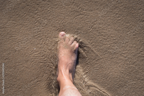 High angle shot of a person's foot on a wet sandy ground