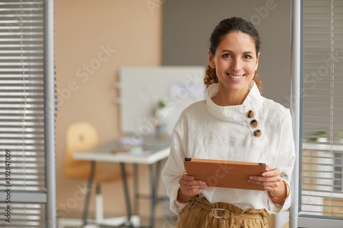 Waist up portrait of smiling successful businesswoman looking at camera and holding digital tablet while working from home, copy space photo