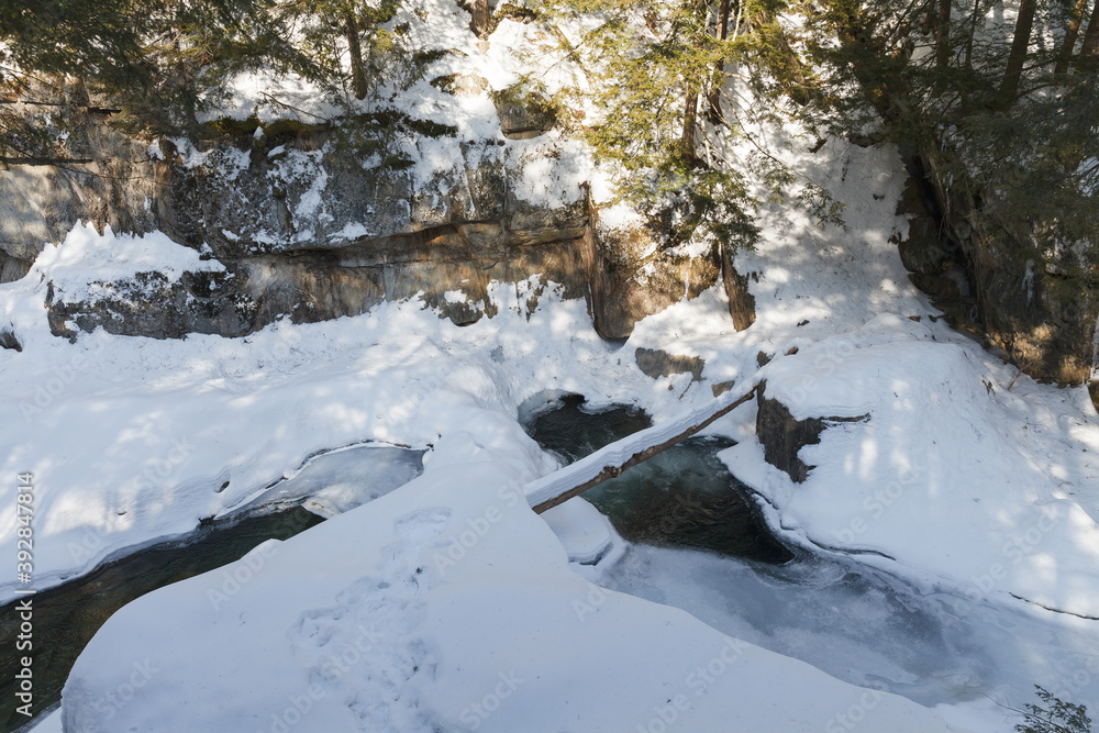 Warren falls - frozen creek under ice and snow with rocky shores. Sunny winter day