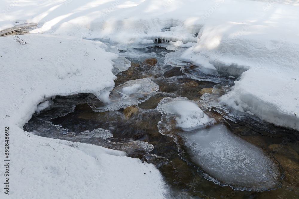 Warren falls - frozen creek under ice and snow with rocky shores. Sunny winter day